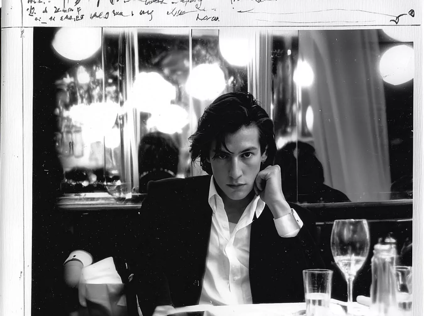 Black and white mens fashion portrait by James Nader photographed at a restaurant table with mirrors and glassware