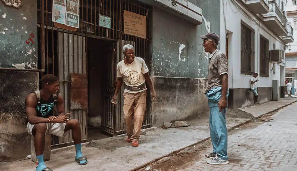 Three men interacting on a narrow residential street in Havana, an example of candid documentary photography