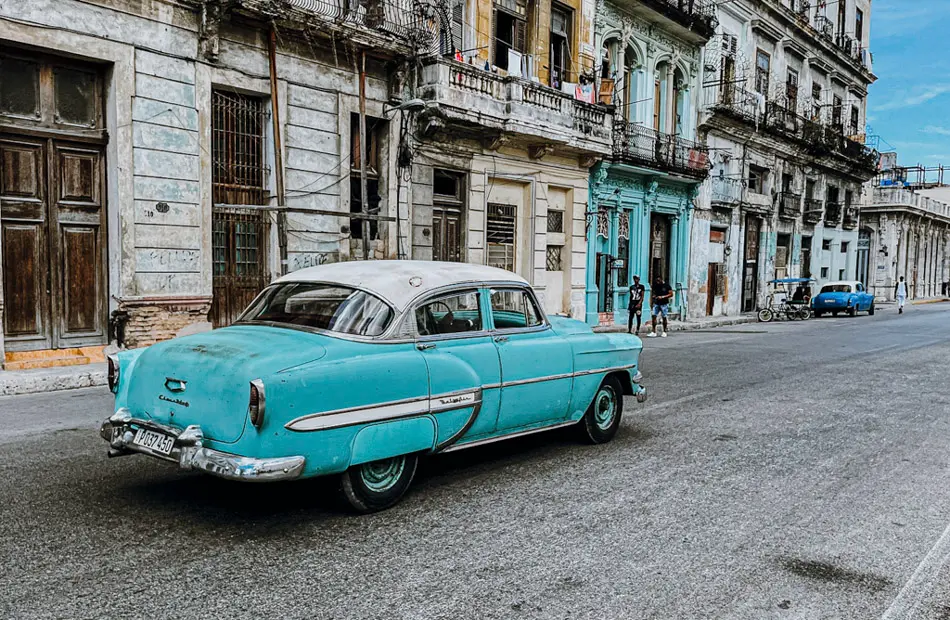 Turquoise classic American car parked outside ageing colonial architecture on a Havana street